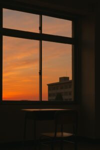 夕焼けに染まる教室で、窓際に置かれた机と椅子が静かに佇んでいる