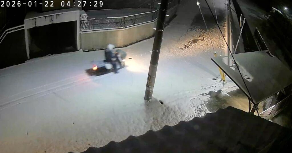 Active snowfall on a quiet residential road near Nishishowadadai campus late at night.